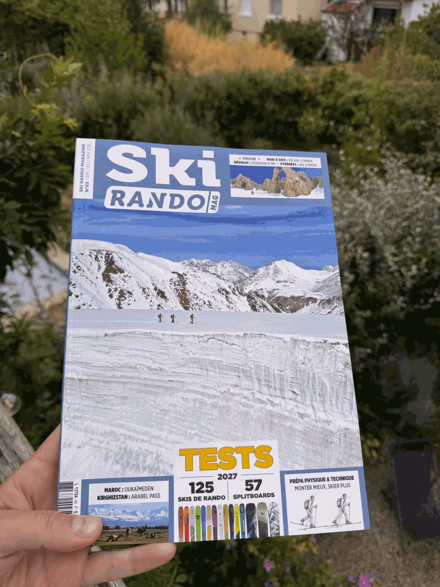 Le Ski Rando Magazine n°65 tenu en main dans un jardin : couverture annonçant les tests 2027 de 125 skis de rando et 57 splitboards, et la prépa physique et technique