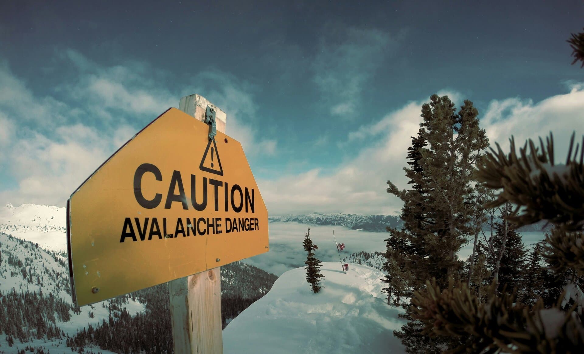 Panneau Caution Avalanche Danger sur une crête enneigée avec vue sur les montagnes